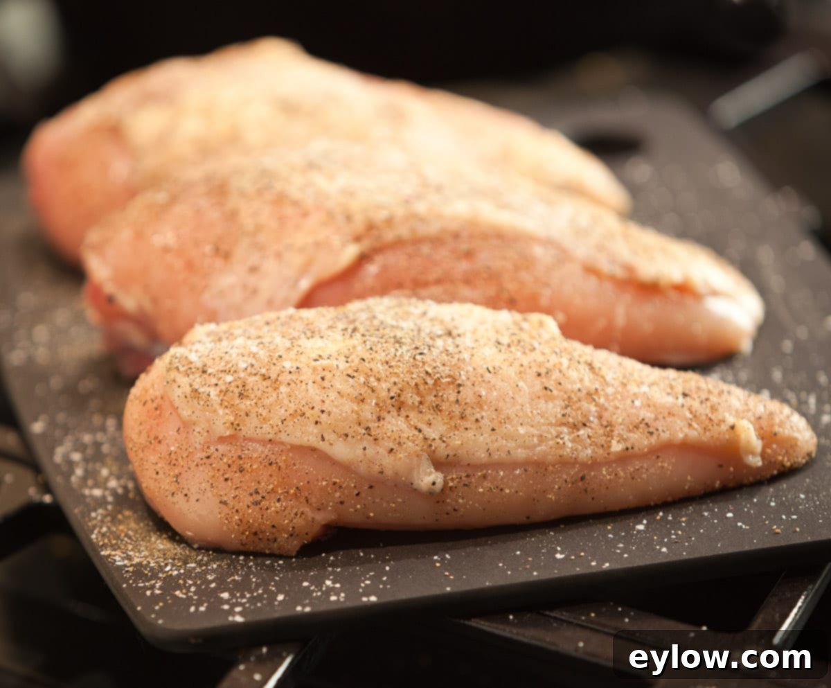 Roast Chicken -4939 Seasoned raw chicken breast on a black cutting board, ready for searing.