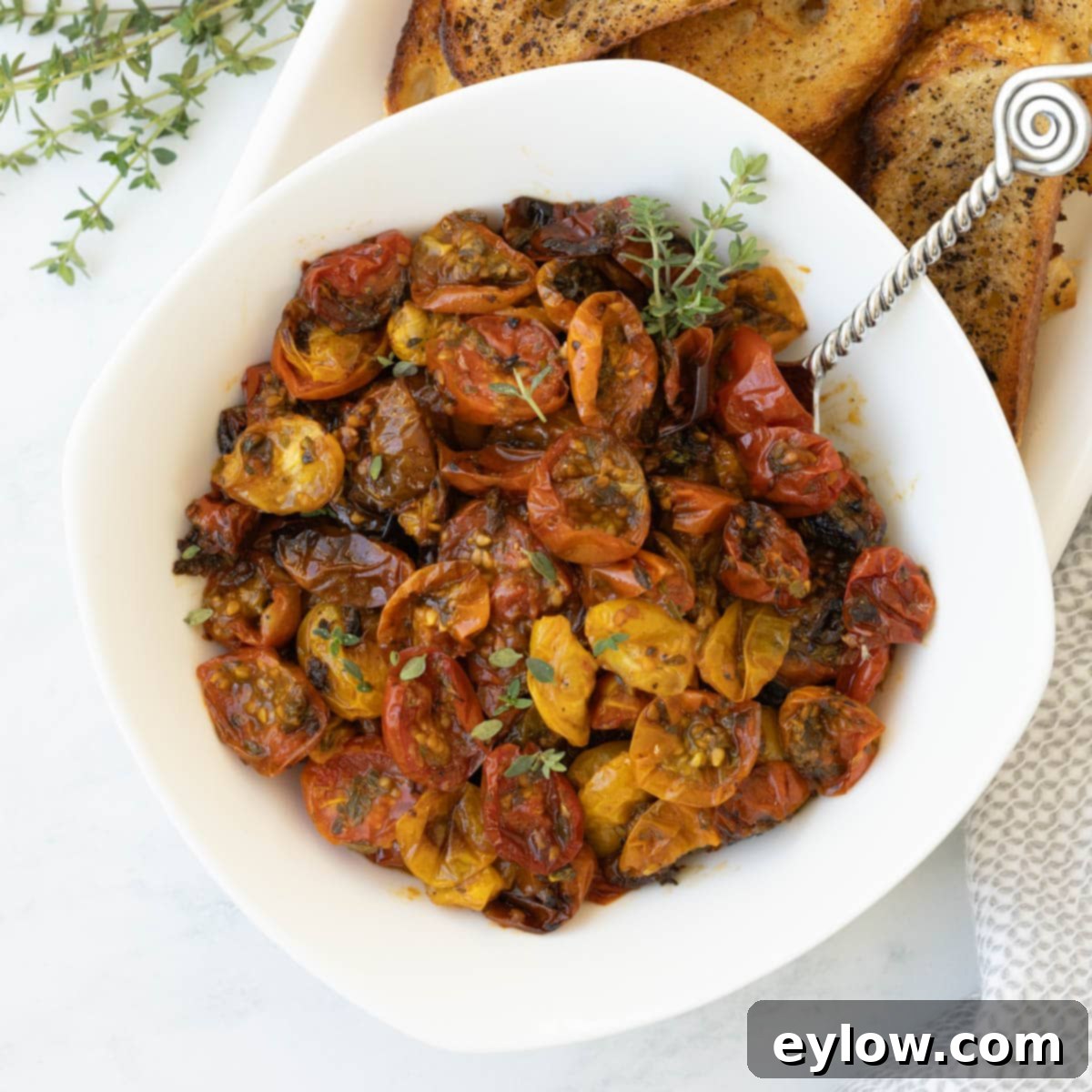 A white bowl of red and gold roasted cherry tomatoes with fresh thyme leaves, showcasing the vibrant and concentrated flavors after roasting.