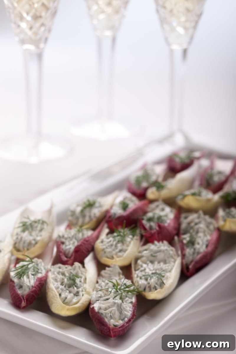 Crisp Belgian endive leaves filled with creamy green herbed cream cheese, artfully arranged on a white serving platter with a garnish of fresh herbs, ready to be served as an elegant appetizer.