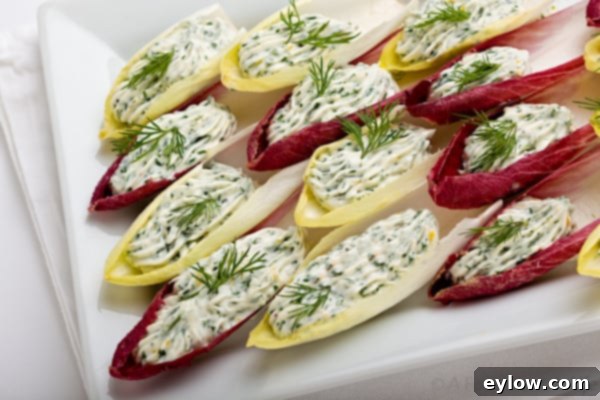 A close-up shot of several individual stuffed endive appetizers, showcasing the vibrant green herbed cream cheese filling beautifully piped into the crisp endive leaves on a white platter.