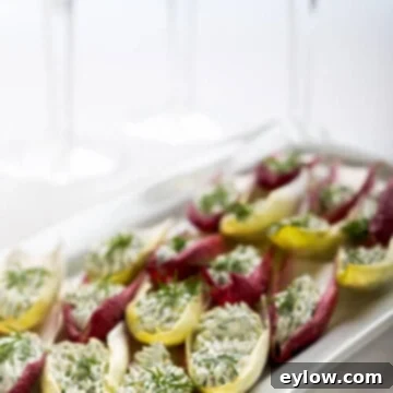 Elegant Belgian endive leaves filled with a creamy green goddess inspired herbed cream cheese, presented beautifully on a platter for an appetizer.