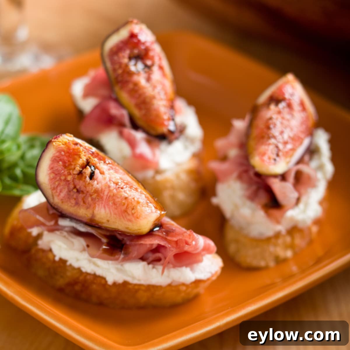 Fig and goat cheese crostini with Prosciutto on a plate, garnished with fresh basil.