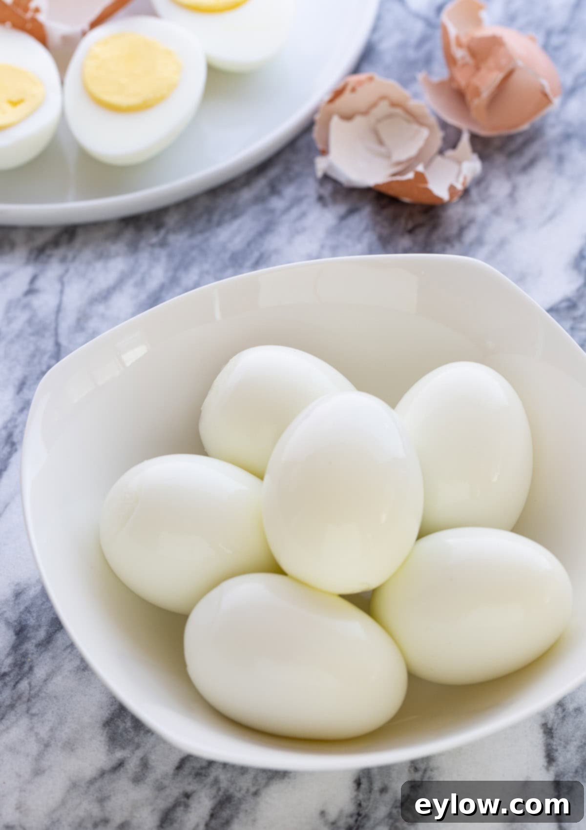The Ultimate Deviled Eggs 4 A small white bowl of peeled hard boiled eggs with egg shells in the back.