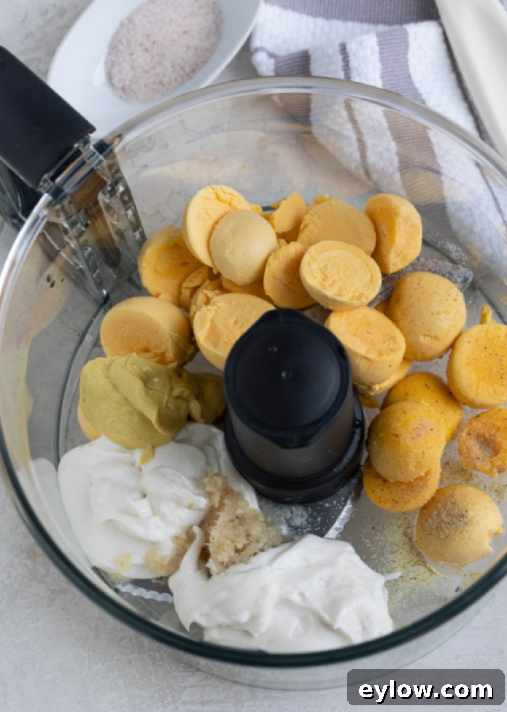 The Ultimate Deviled Eggs 6 Golden egg yolks, mustard, mayonnaise, and horseradish in a food processor work bowl.