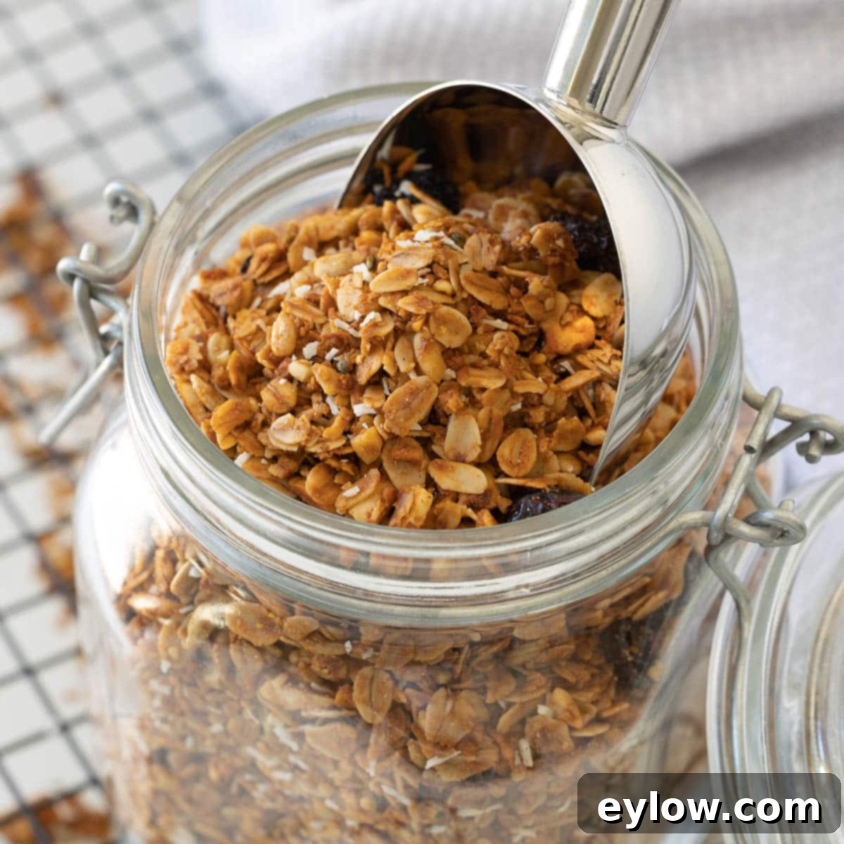 A close up of an open jar of homemade granola with a silver scoop.