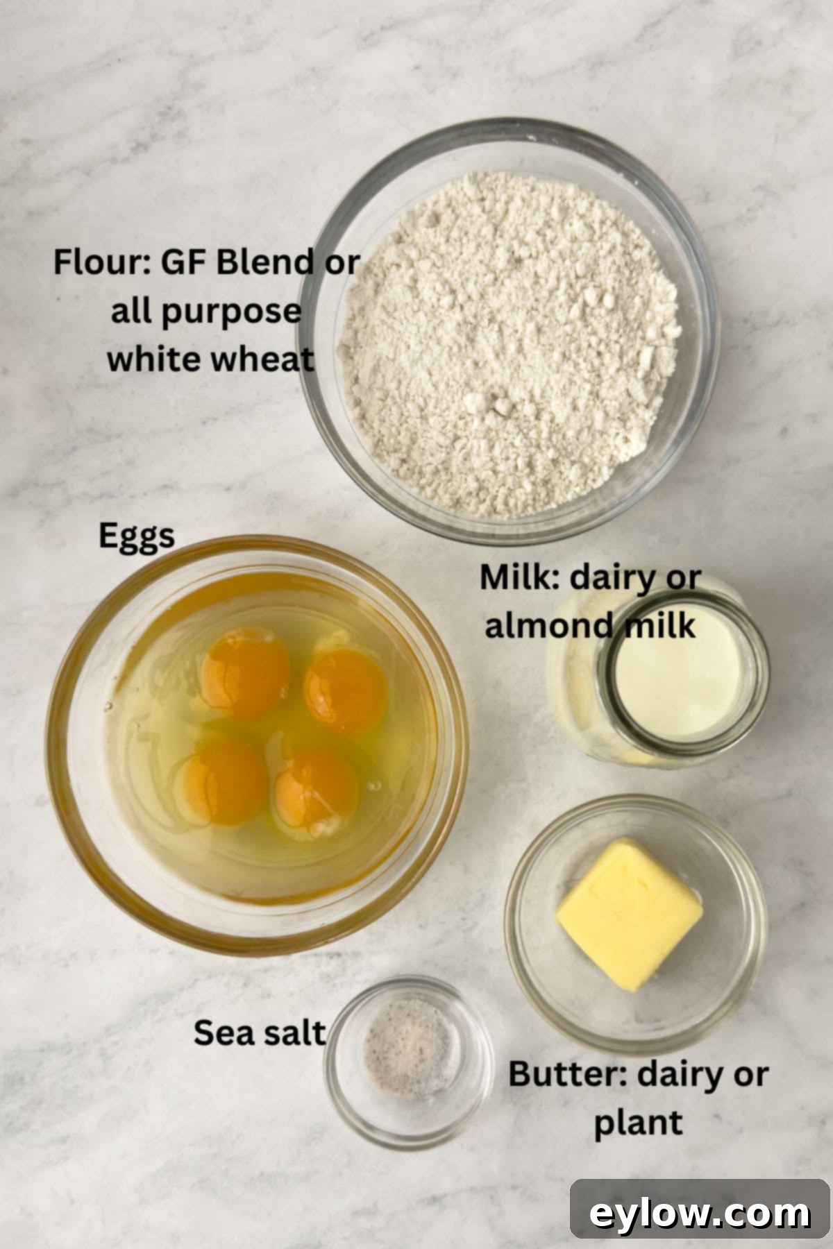 Gluten-Free Dutch Baby German Pancakes 3 Simple ingredients for a Dutch baby pancake in bowls on the counter, including flour, eggs, milk, and butter, ready for preparation.