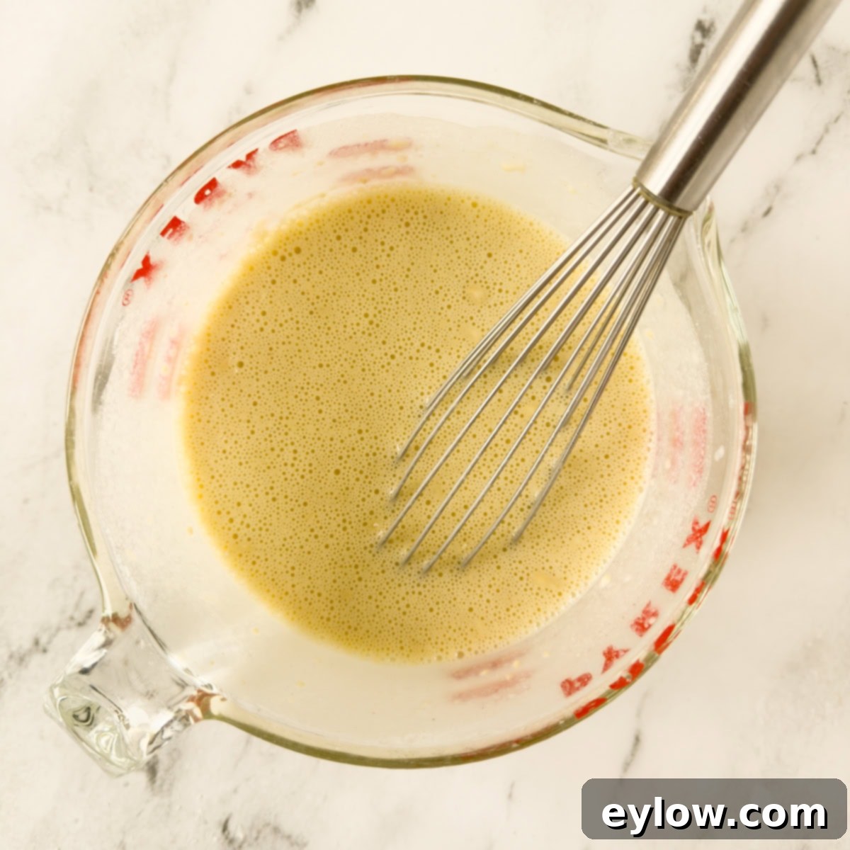 Gluten-Free Dutch Baby German Pancakes 5 Smooth batter for a Dutch baby pancake with a whisk in a glass measuring container, showing perfect consistency.
