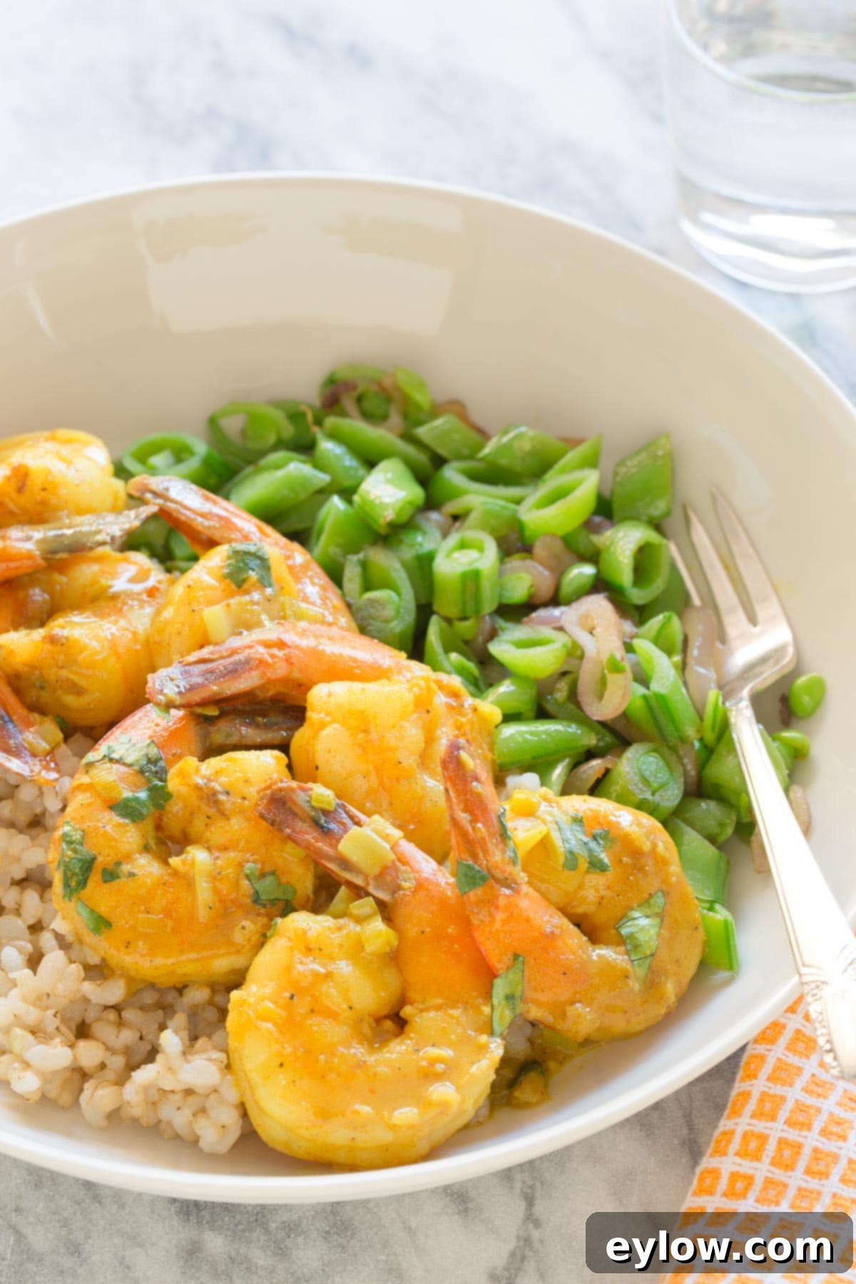 Effortless Coconut Shrimp Curry 5 A vibrant bowl of coconut curry shrimp served over fluffy white rice, garnished with fresh snap peas and cilantro.
