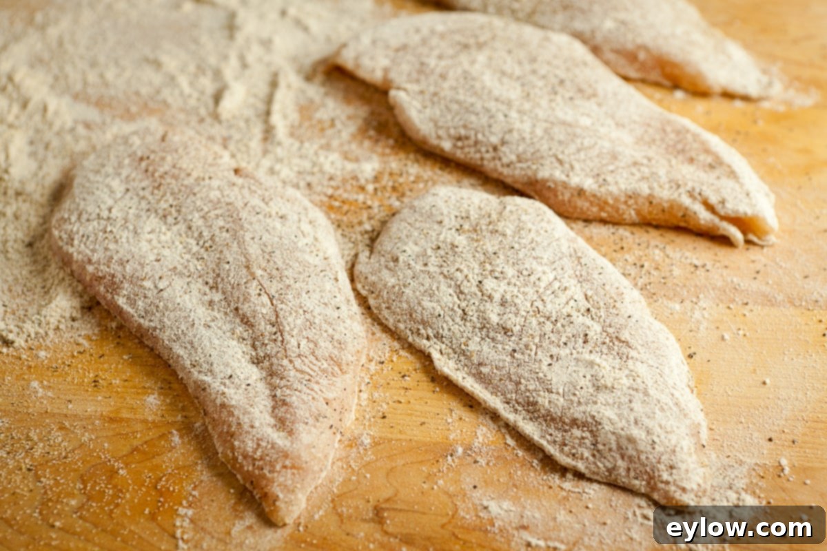 Dusting thinly sliced chicken cutlets with a light coating of flour to prepare them for cooking, ensuring a crisp golden exterior.