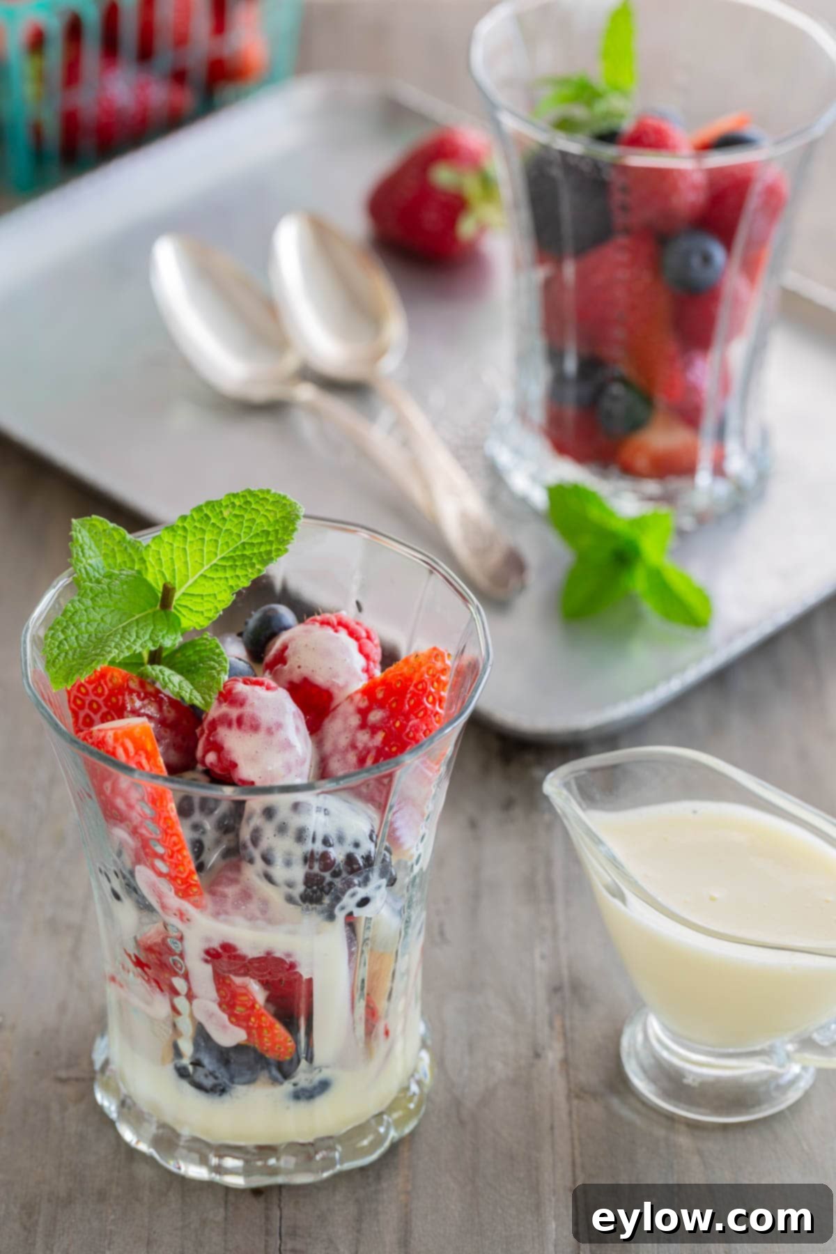 A glass filled with fresh berries drizzled with sabayon dessert sauce and topped with mint.
