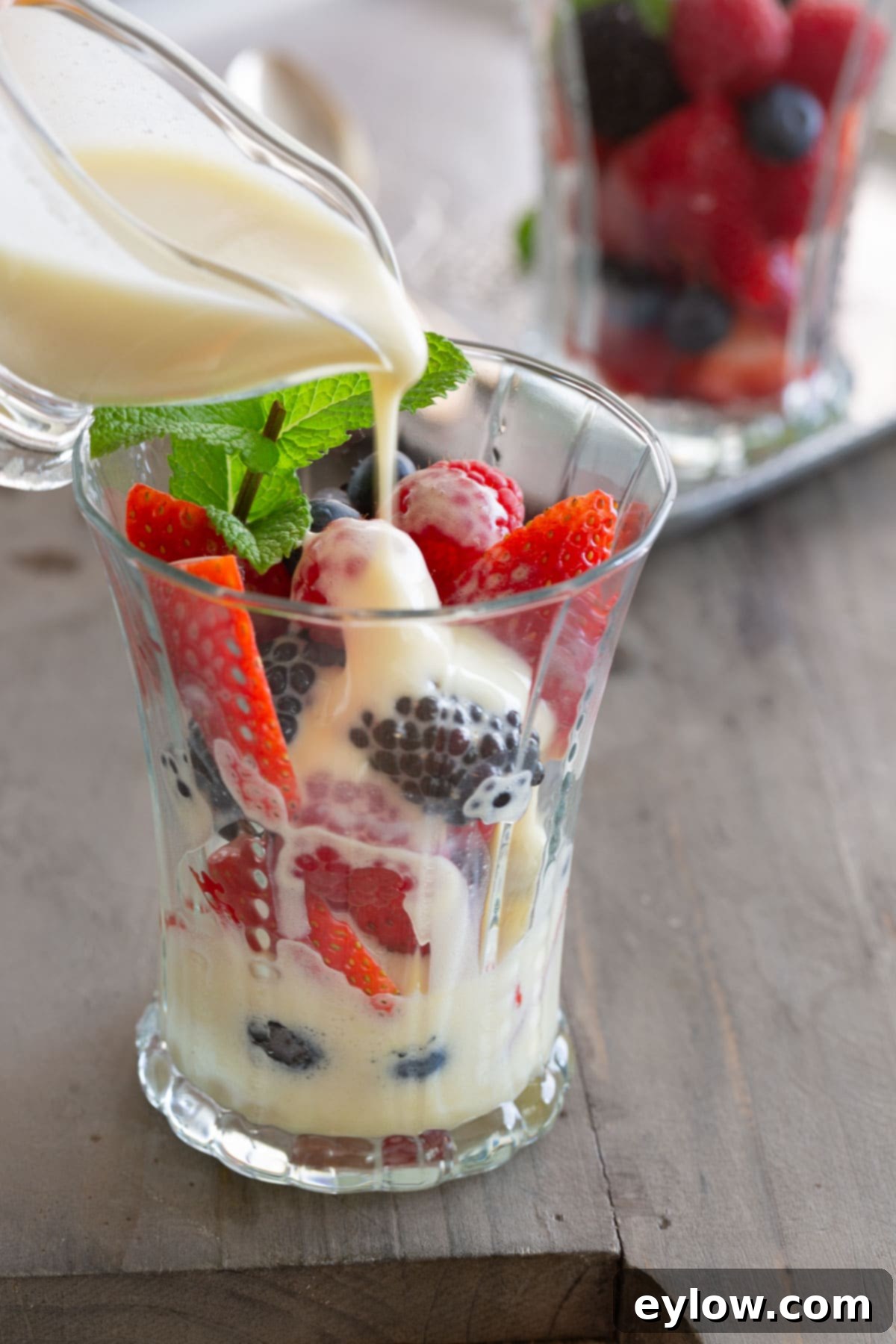 A glass pitcher with sabayon pouring into a dessert glass filled with colorful fresh berries.