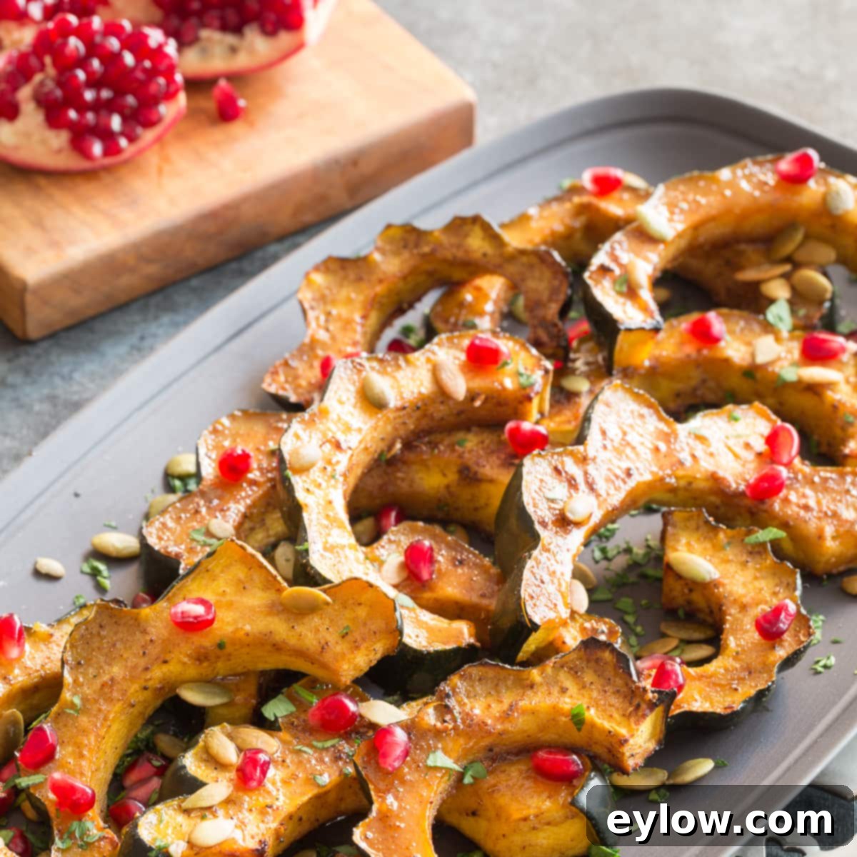 Maple roasted acorn squash slices arranged beautifully on a gray platter with pomegranate seeds scattered on top.