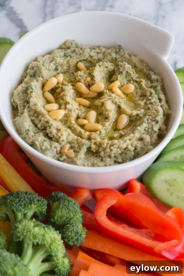 Creamy hot artichoke dip served in a rustic bowl, garnished with fresh herbs and toasted pine nuts.