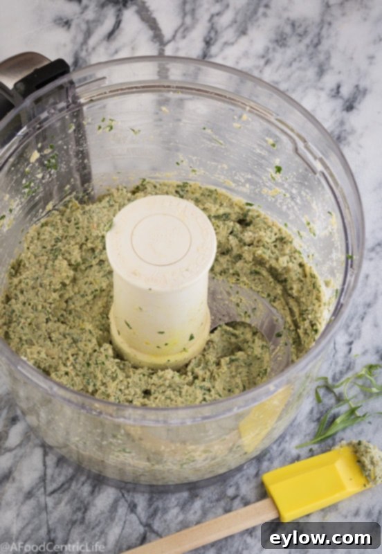 Smoothly pureed hot artichoke dip in a food processor bowl with the blade, demonstrating readiness for baking or serving.