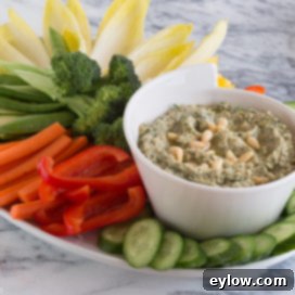A bowl of hot artichoke dip, garnished with fresh herbs and a wooden spoon, ready to be served.