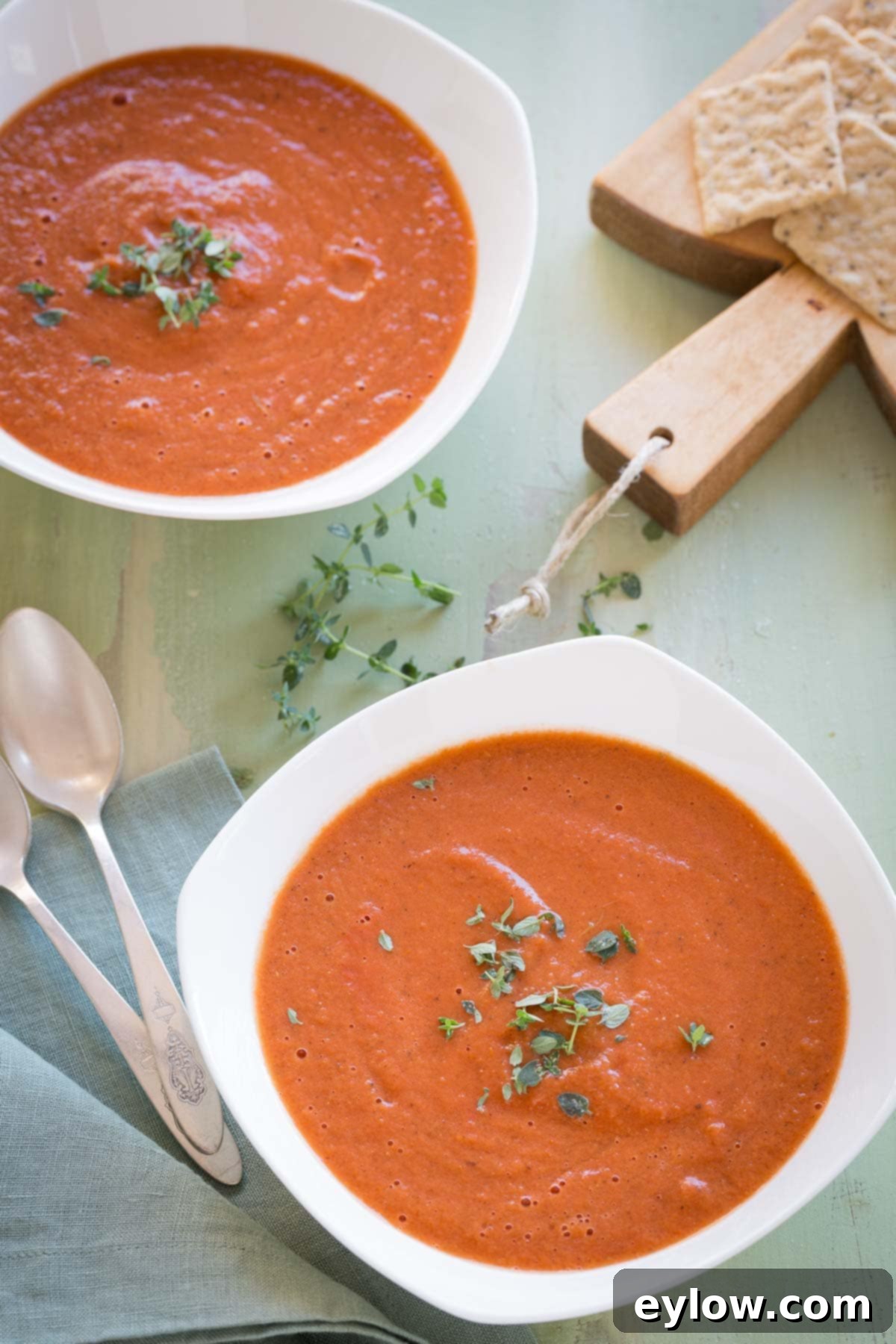 Two bowls of creamy homemade tomato soup in white bowls with crackers beside.