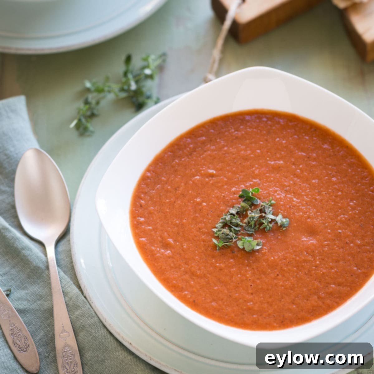 A single bowl of tomato soup with a sprig of rfesh thyme leaves and silver spoon.