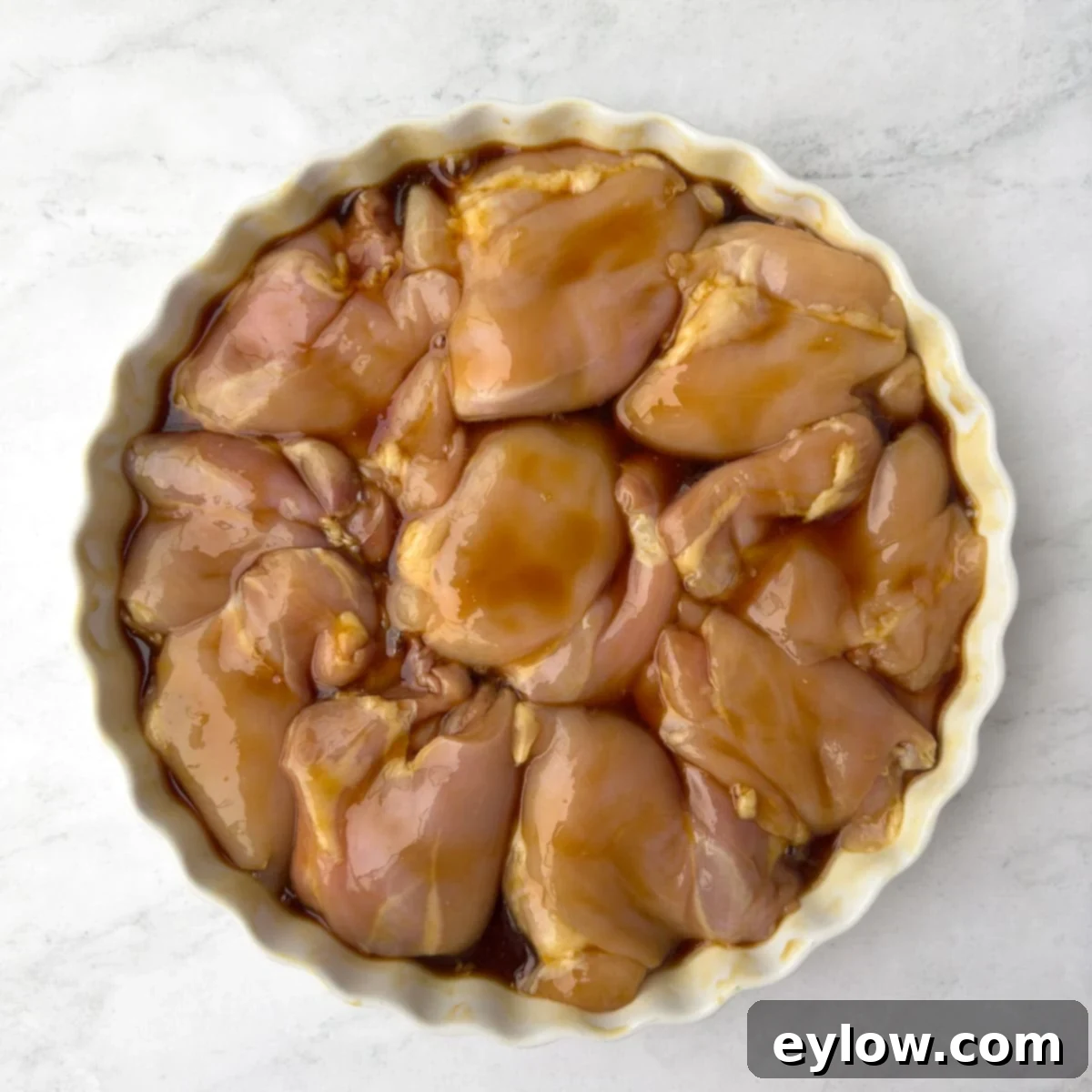 Marinating boneless skinless chicken thighs in teriyaki sauce in a casserole dish.