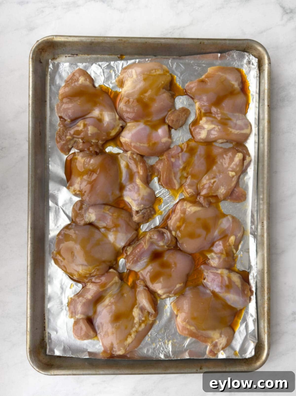 Baking marinated chicken thighs on a foil covered baking sheet. 
