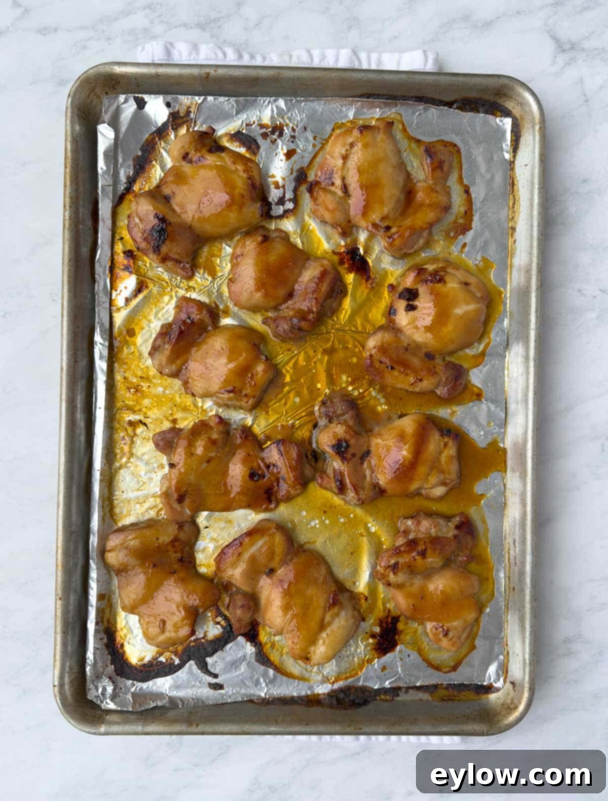 Baked teriyaki chicken on a foil-lined baking sheet, ready to slice. 