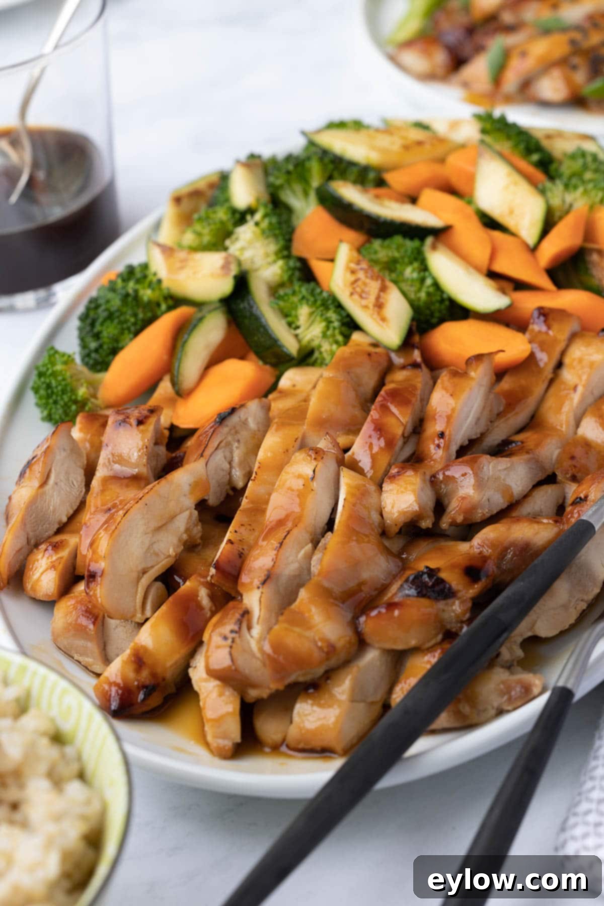 Closeup of golden teriyaki chicken with a glass of teriyaki sauce on the side. 