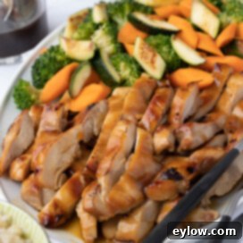 Closeup of golden teriyaki chicken with a glass of teriyaki sauce on the side.