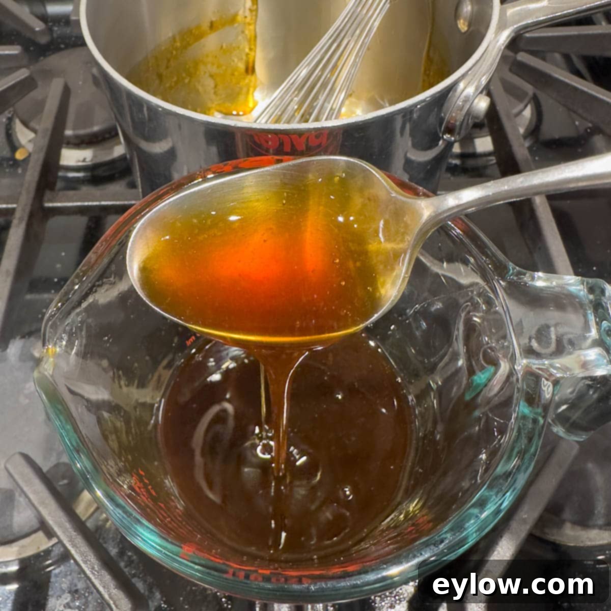 Golden brown finished sauce pouring off a spoon into a container.