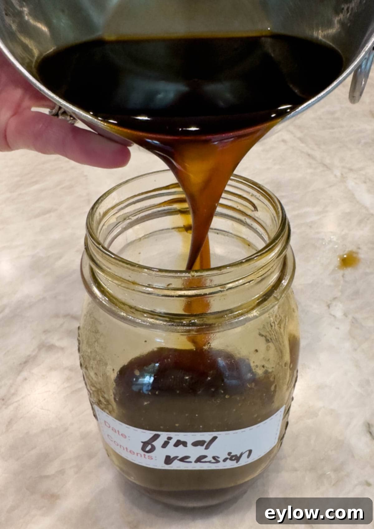 Deep brown finished homemade teriyaki sauce being poured into a jar for storage.