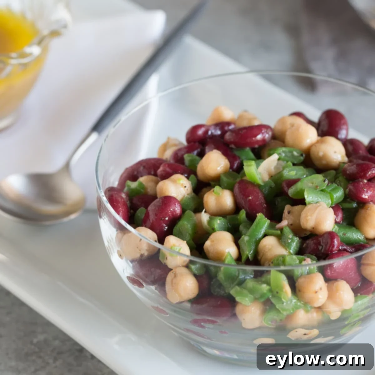 Effortless Zesty Three Bean Salad 11 Colorful 3-bean salad in a glass bowl with a serving spoon.