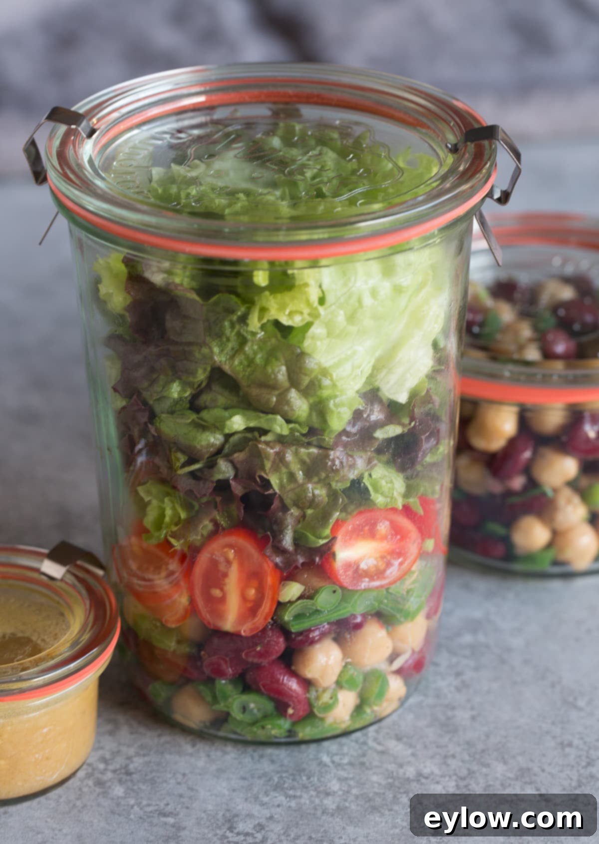 Effortless Zesty Three Bean Salad 12 A tall jar of meal prepped bean salad with lettuce, tomatoes and dressing.