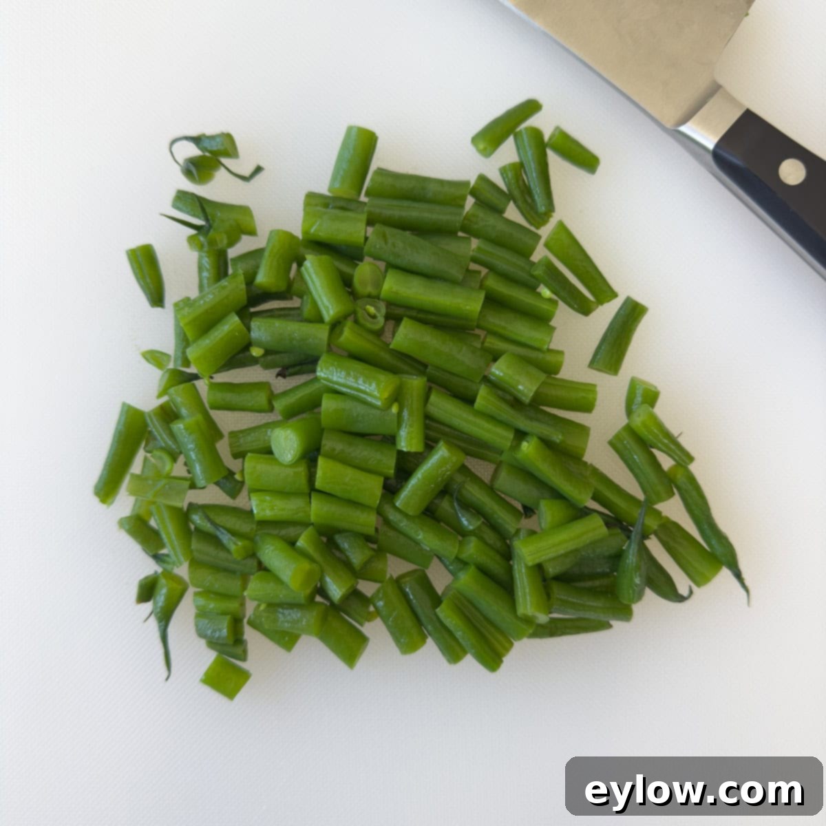 Effortless Zesty Three Bean Salad 7 Chopped green beans on a white cutting board with a knife.