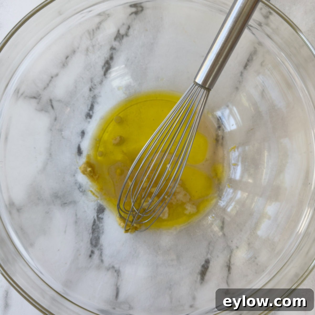 Effortless Zesty Three Bean Salad 10 Ingredients for a vinaigrette in a glass bowl with a steel whisk.