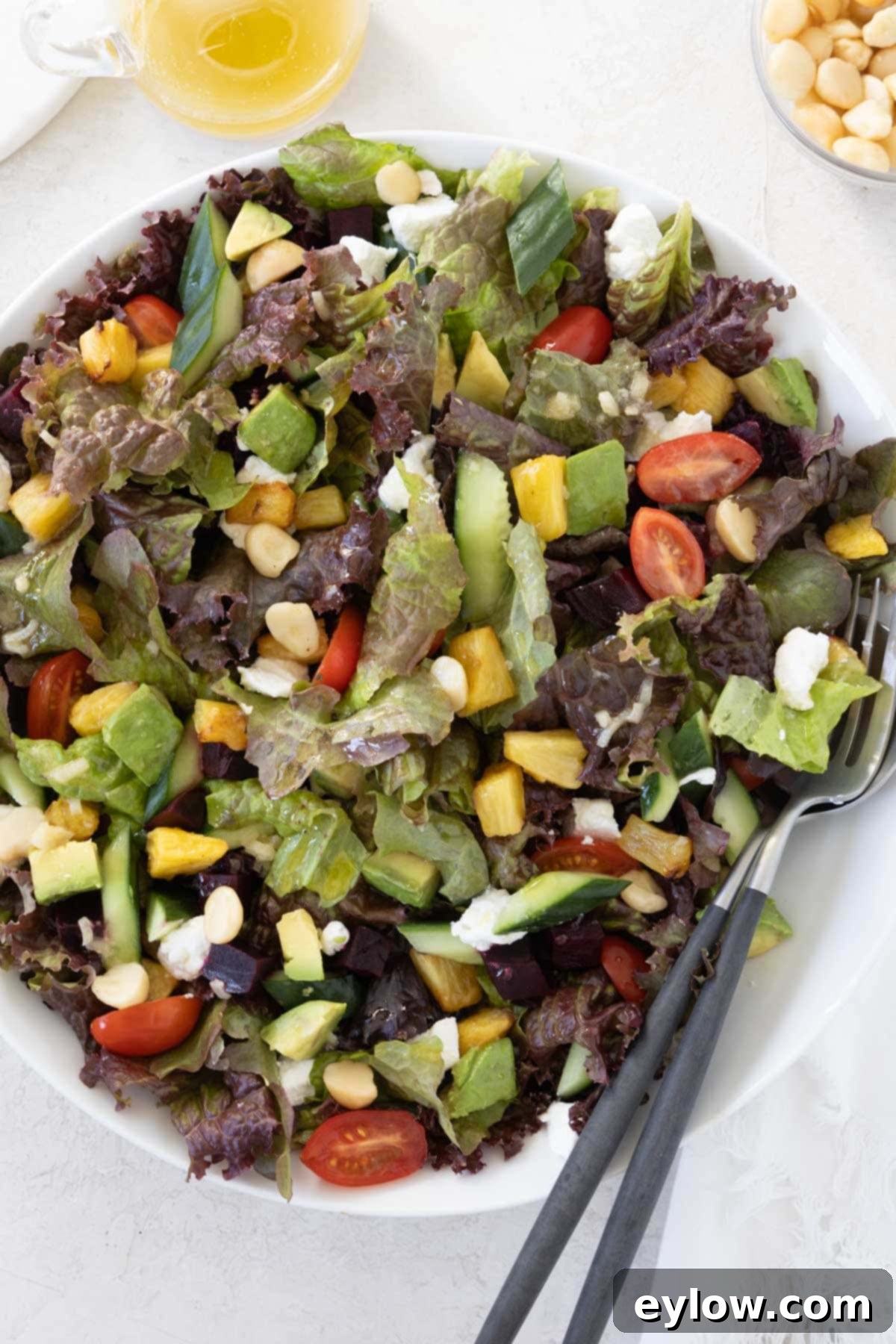 Hawaiian Goat Cheese Salad 2 A large round salad bowl filled with fresh greens, juicy tomatoes, vibrant beets, sweet pineapple, creamy goat cheese, crisp cucumber, crunchy macadamia nuts, and smooth avocado, ready to be enjoyed.