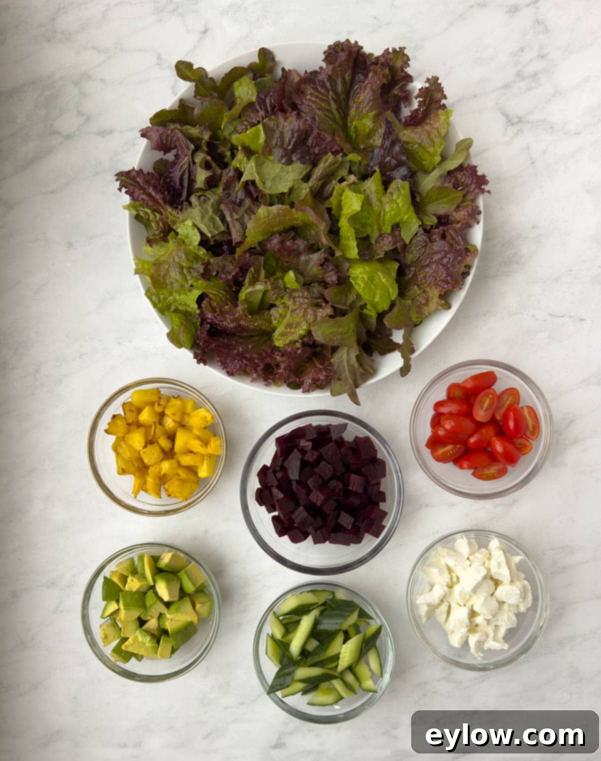 Hawaiian Goat Cheese Salad 4 Various Hawaiian salad ingredients prepped and neatly arranged, including diced pineapple, halved tomatoes, sliced cucumber, crumbled goat cheese, and fresh greens, all ready to be tossed together for serving.