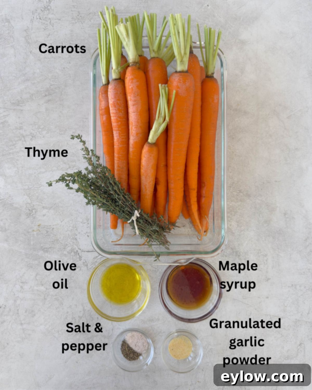 Fresh carrots, olive oil, maple syrup, and fresh thyme on a wooden board.