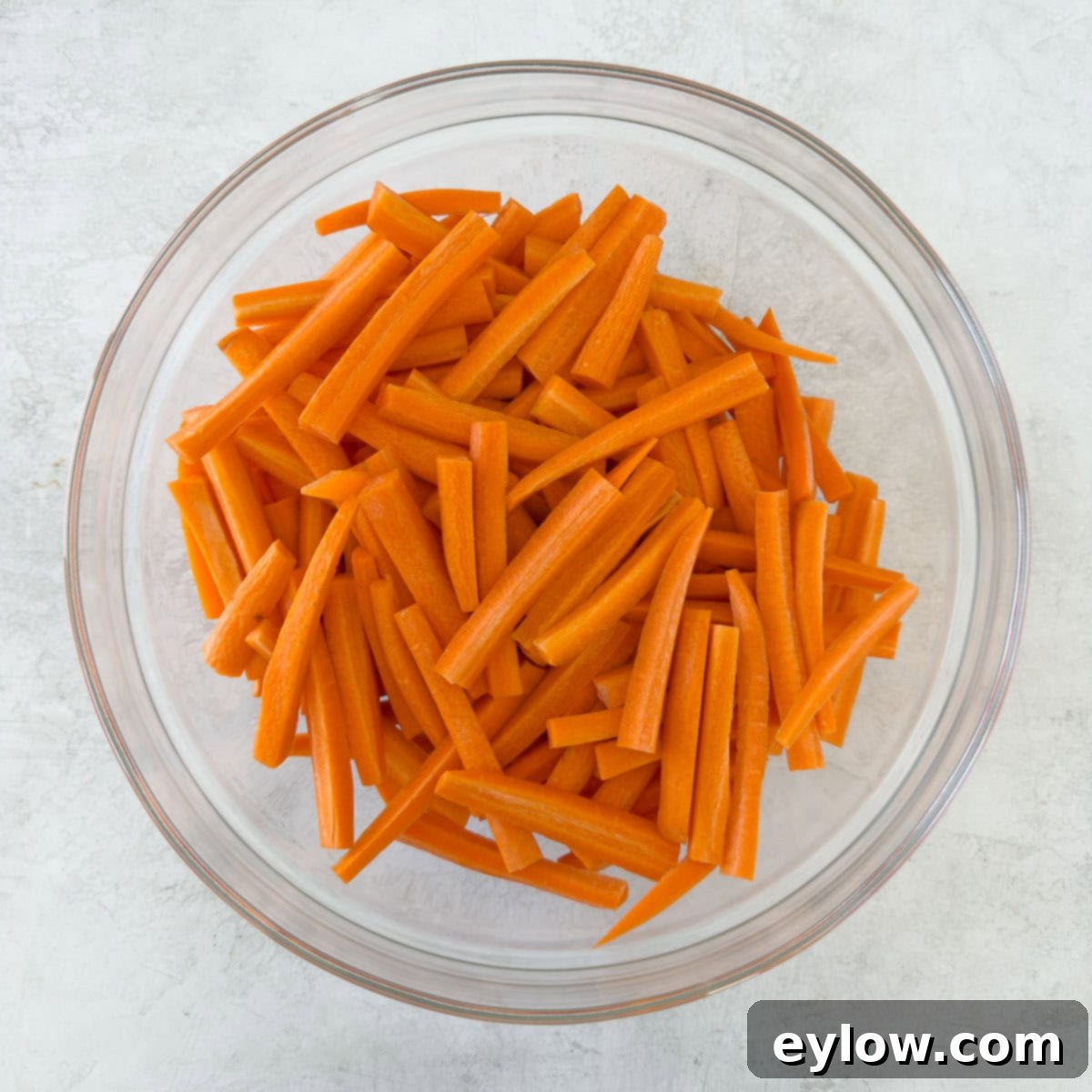 Bright orange carrot sticks in a glass bowl after being peeled and cut.