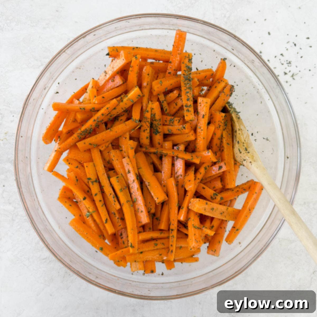 Julienned carrots in a bowl tossed with olive oil, salt, pepper, and fresh thyme leaves, ready for roasting.