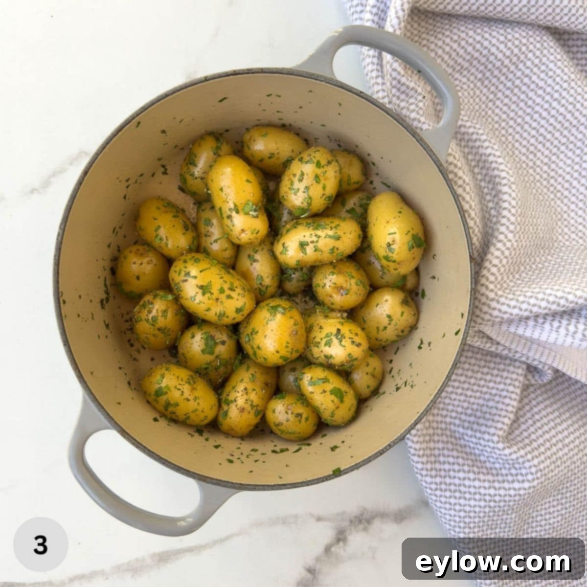Golden Buttered Potato Gems 6 Cooked baby potatoes covered in fresh herbs in a pot.