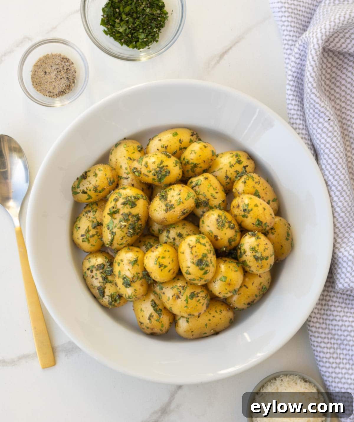 Golden Buttered Potato Gems 7 Herbed baby potatoes in a white bowl at the table for serving.