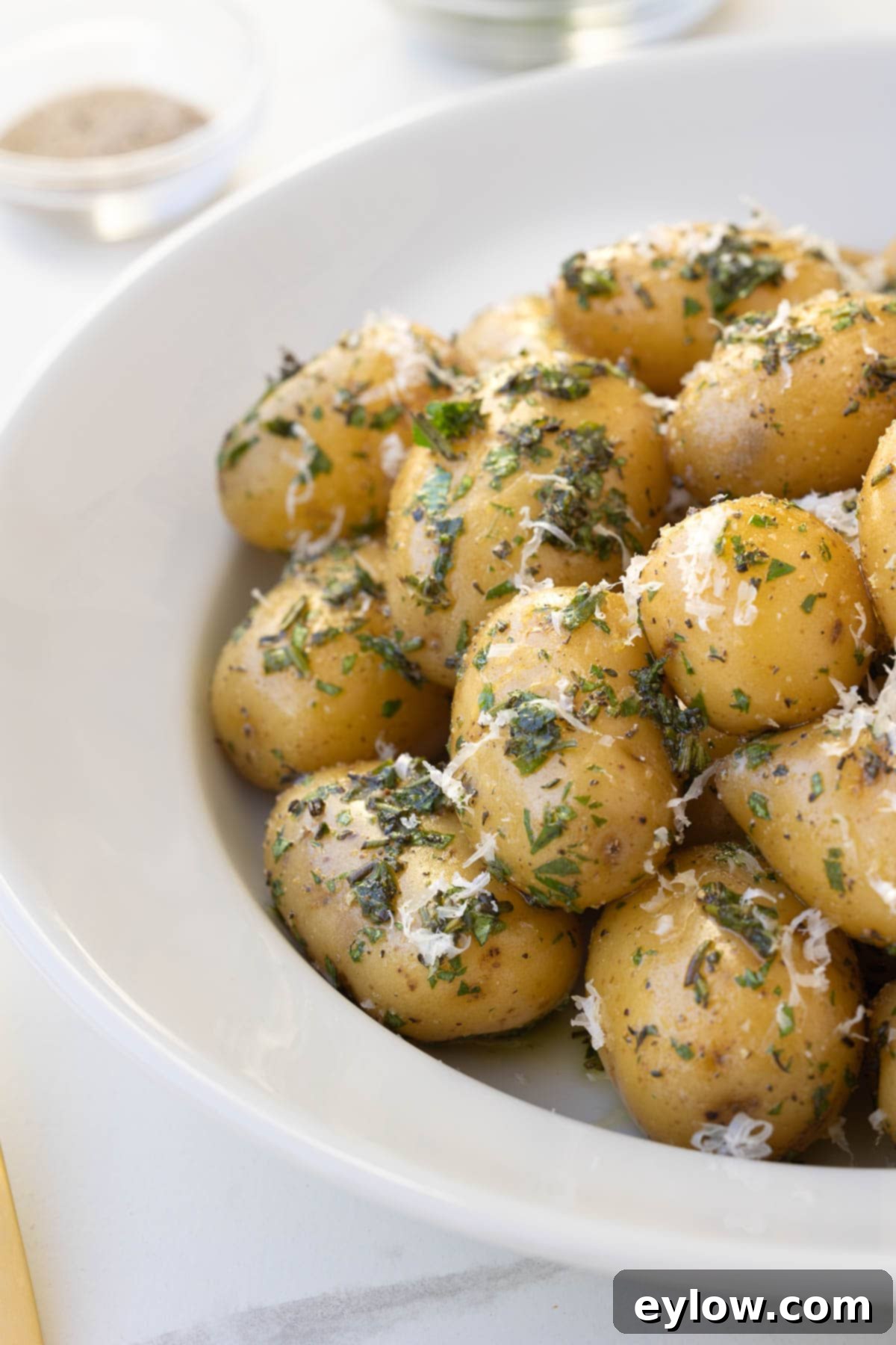 Golden Buttered Potato Gems 8 At the table, a white bowl of golden herbed baby Dutch potatoes wtih herbs and Parmesan.