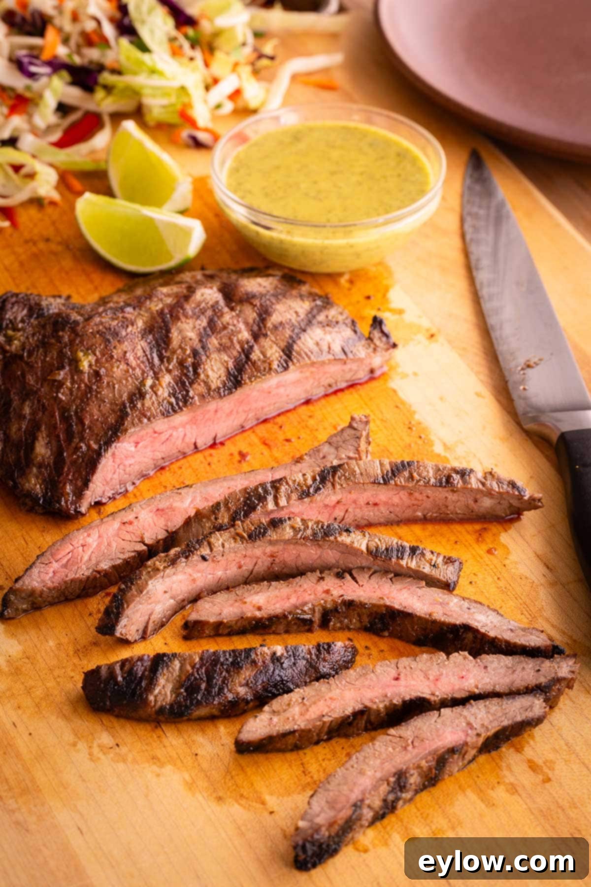 Sliced flank steak on a cutting board with flank steak marinade in a bowl.