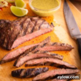Sliced flank steak on a cutting board with flank steak marinade in a small bowl.