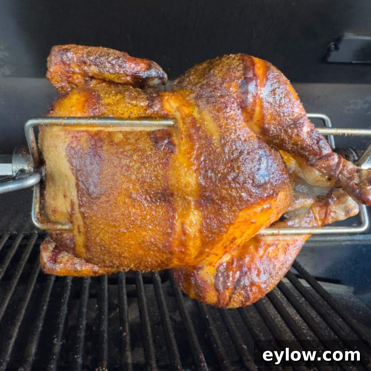 Golden brown rotisserie chicken cooking on a grill with gleaming silver meat forks, showing its crispy skin.