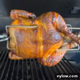 Golden brown chicken on a rotisserie grill with silver meat forks, perfectly cooked.