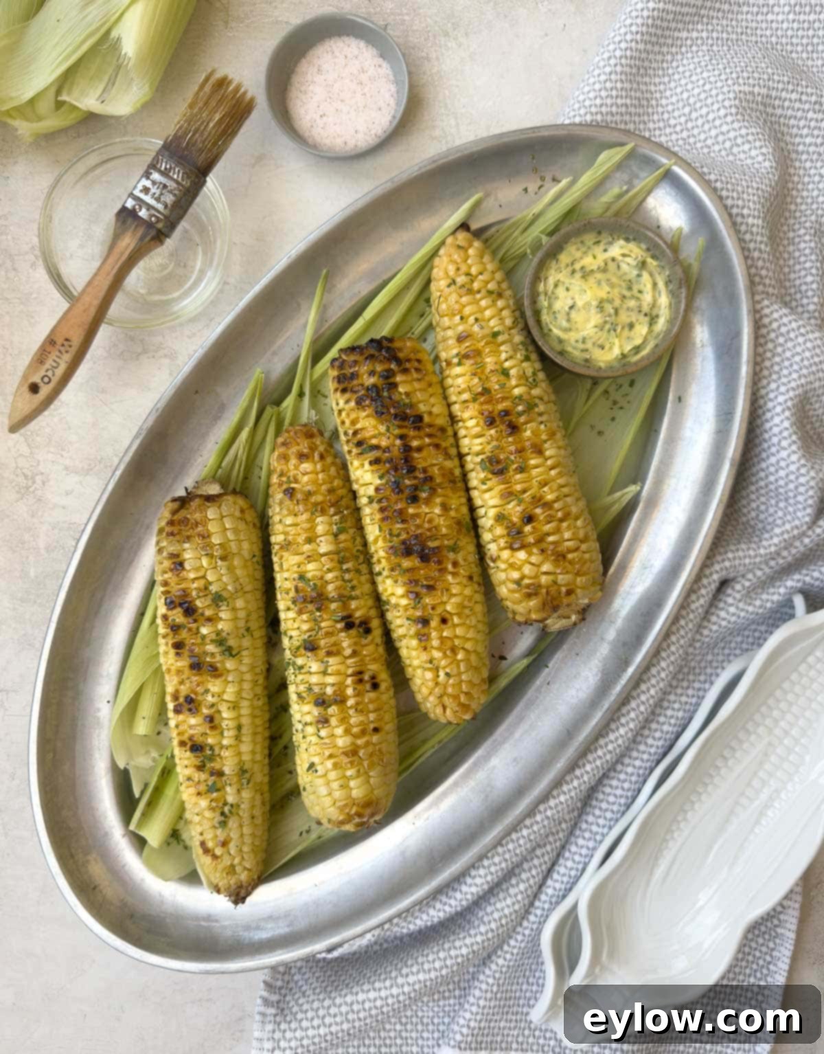 A pewter platter of golden grilled corn with herb butter. 