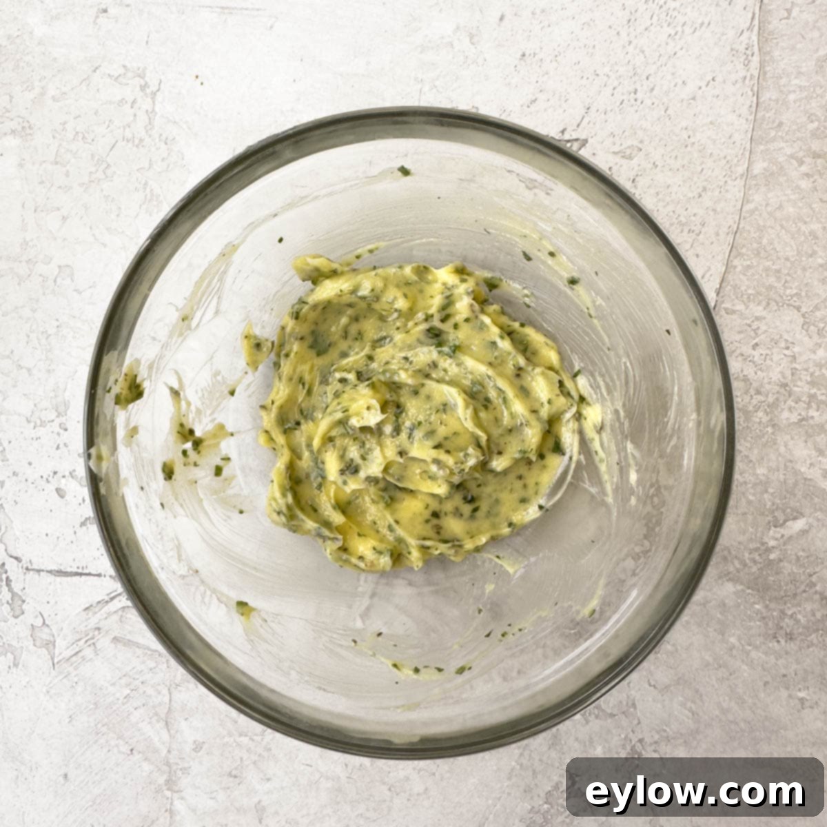 A bowl of creamy yellow garlic herb butter. 