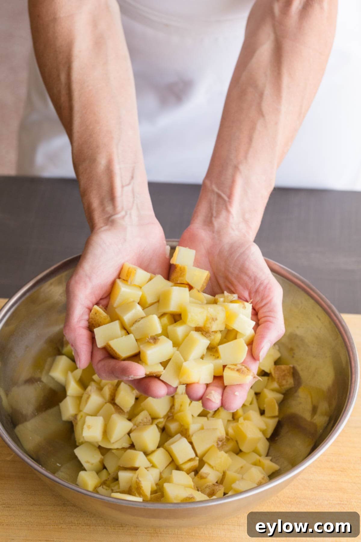 Chef's hands carefully dicing perfectly cooked, cubed potatoes over a large mixing bowl for potato salad preparation.
