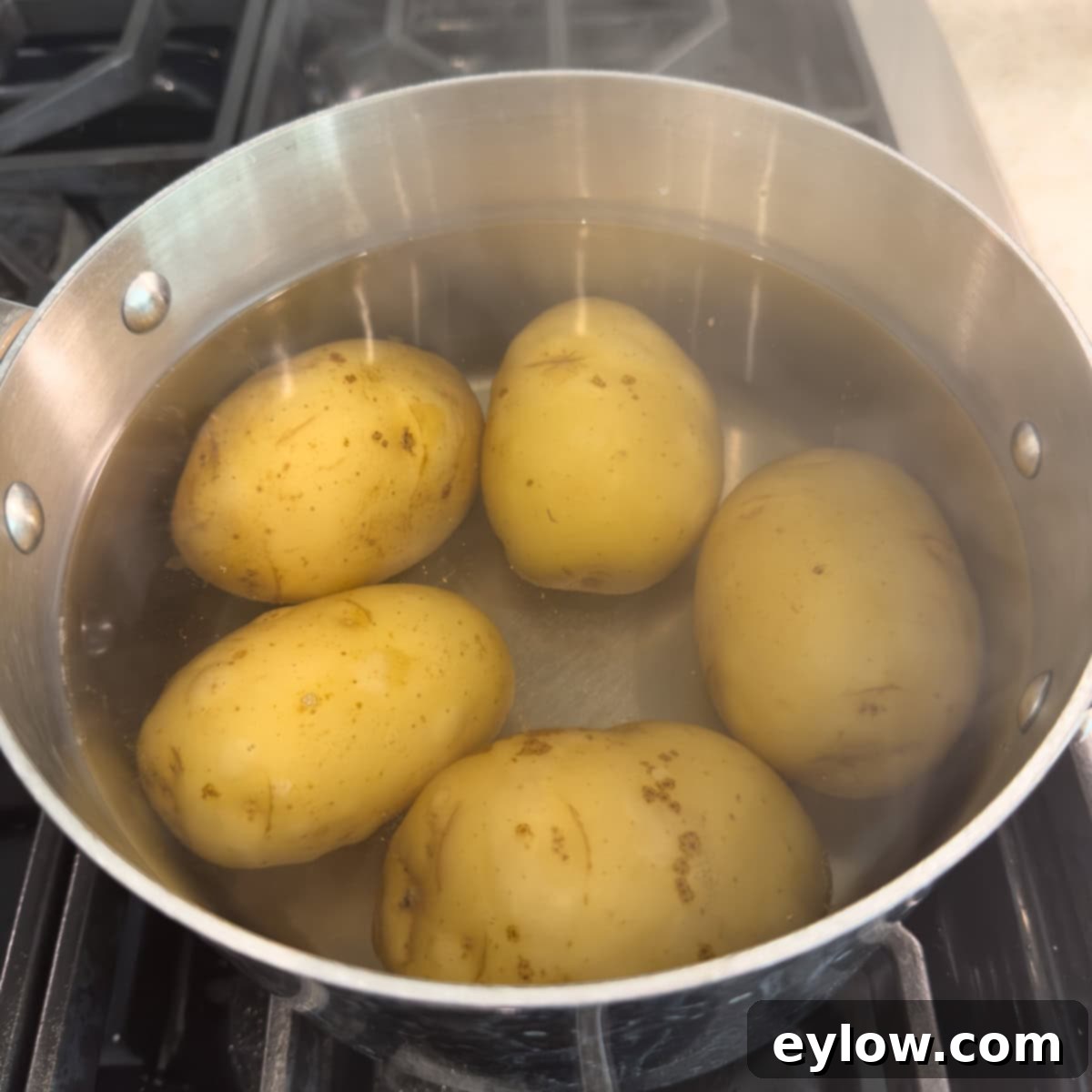 Whole, unpeeled potatoes simmering gently in a large pot of salted water, ready for making potato salad.