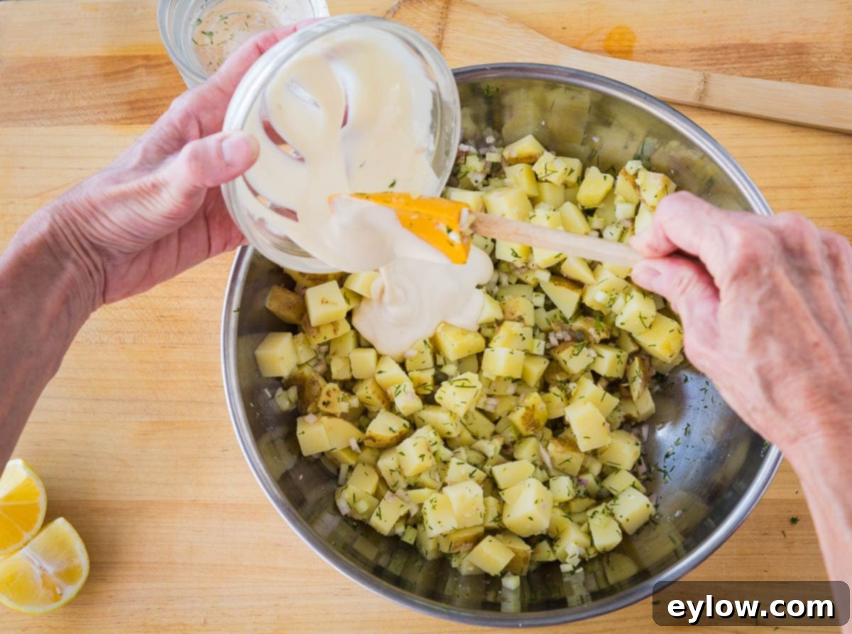 A stream of creamy mayonnaise being drizzled over a bowl of potato salad, marking the final step of preparation before serving.