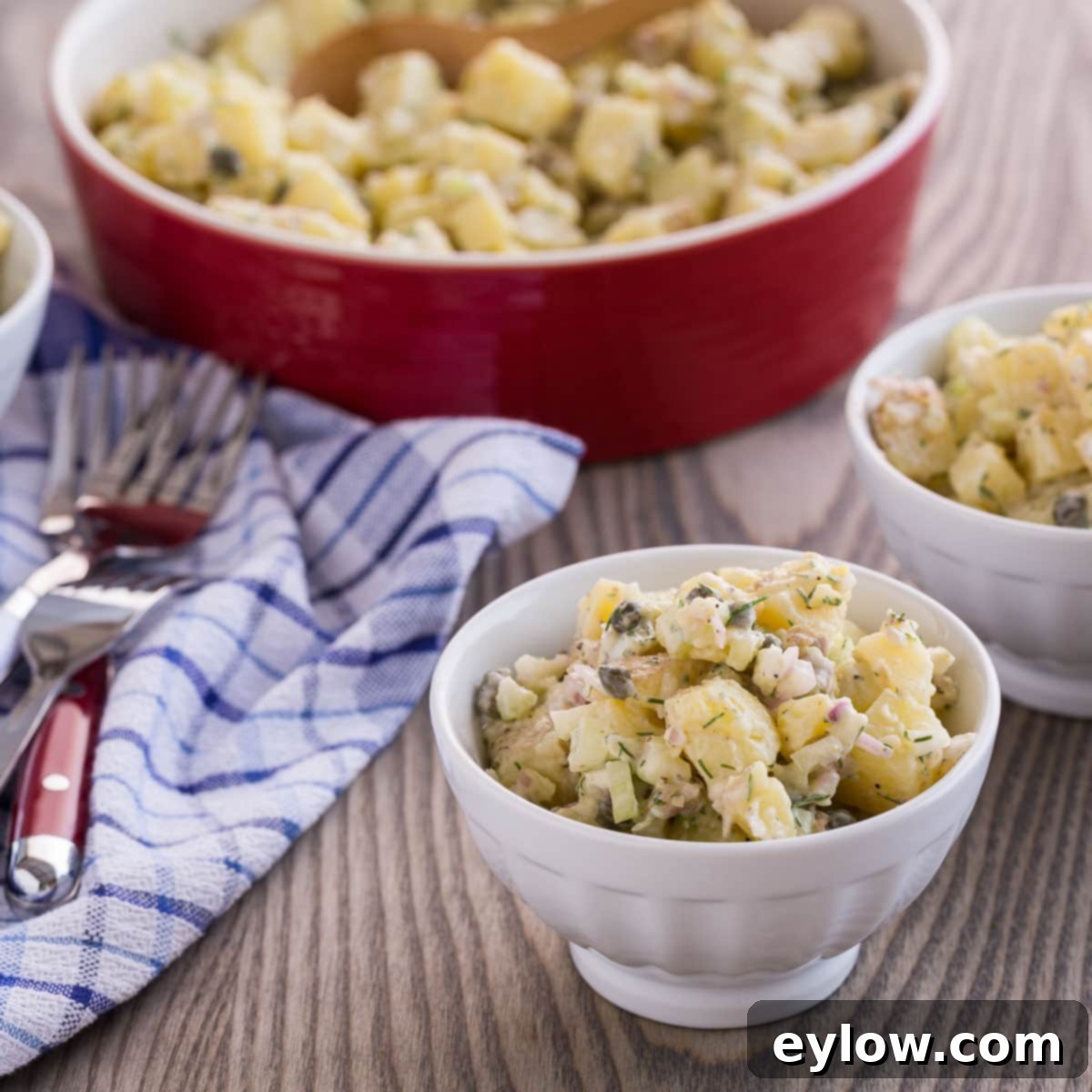 Individual small white bowls filled with creamy French potato salad, garnished with fresh herbs, ready for serving with forks.